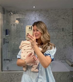 Woman holding a baby in a bathroom taking a mirror selfie.