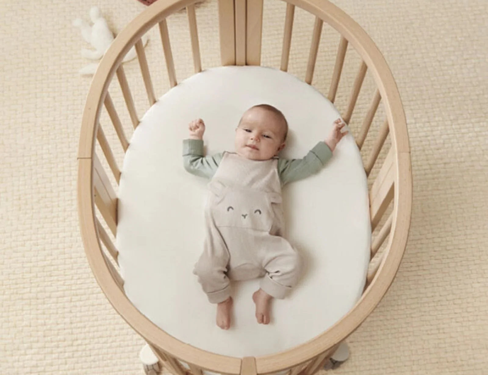 Stokke Sleepi Mini Mattress in white with a baby lying on their back with arms outstretched, seen from above in the bed