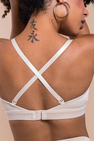 Woman wearing a beige bralette with criss-cross straps on a beige background