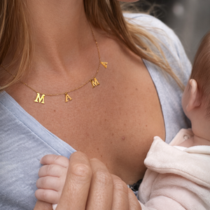 Woman wearing a gold necklace with letter charms, holding a baby.