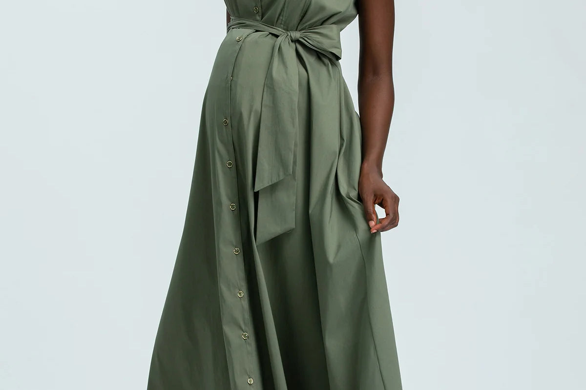 Woman wearing green sleeveless full length shirt dress on pale background