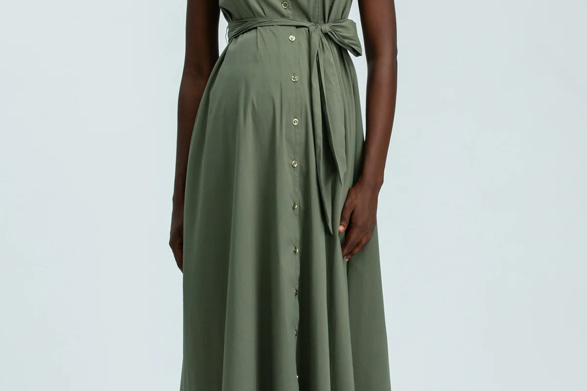 Woman wearing green sleeveless full length shirt dress on pale background