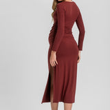 A woman modeling a long-sleeve, ruched midi dress in a deep burgundy or rust red color, shown from a three-quarters back view against a light gray studio background.