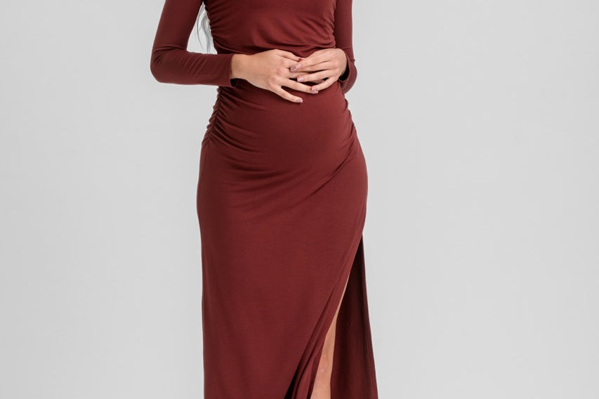 A woman modeling a long-sleeve, crew-neck wrap-style midi dress in a deep burgundy color, standing against a solid light gray studio background.