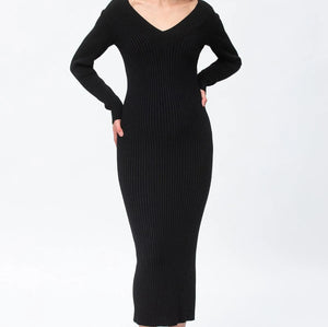 A woman modeling a black ribbed long-sleeve V-neck midi dress with taupe ankle boots against a plain white studio background.