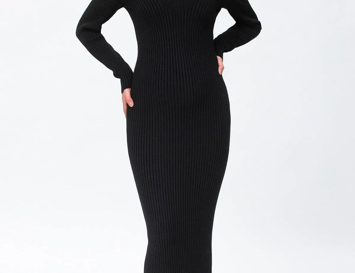 A woman modeling a black ribbed long-sleeve V-neck midi dress with taupe ankle boots against a plain white studio background.