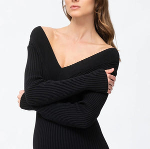 A woman modeling a black ribbed knit off-the-shoulder sweater dress against a plain white studio background.