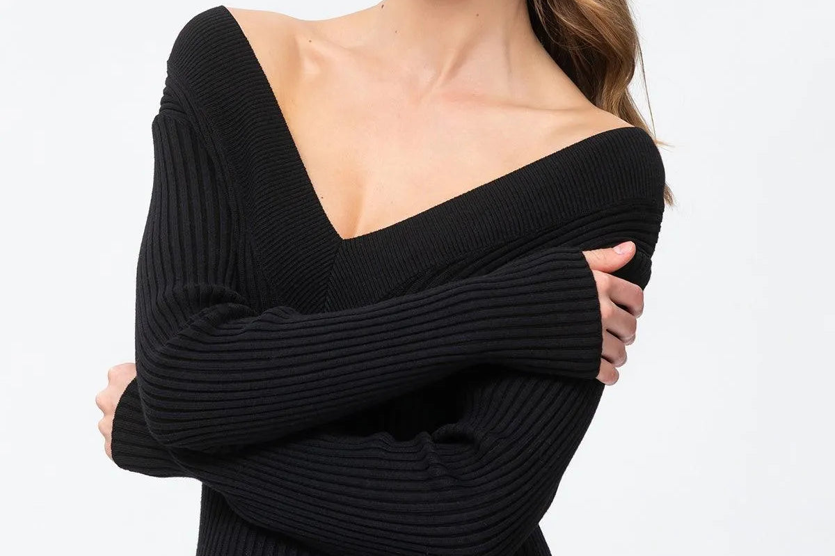 A woman modeling a black ribbed knit off-the-shoulder sweater dress against a plain white studio background.