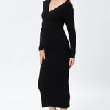 A woman modeling a black ribbed knit long-sleeve midi dress with a V-neckline, paired with taupe ankle boots, against a plain white studio background.
