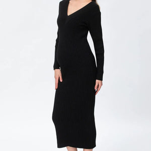 A woman modeling a black ribbed knit long-sleeve midi dress with a V-neckline, paired with taupe ankle boots, against a plain white studio background.