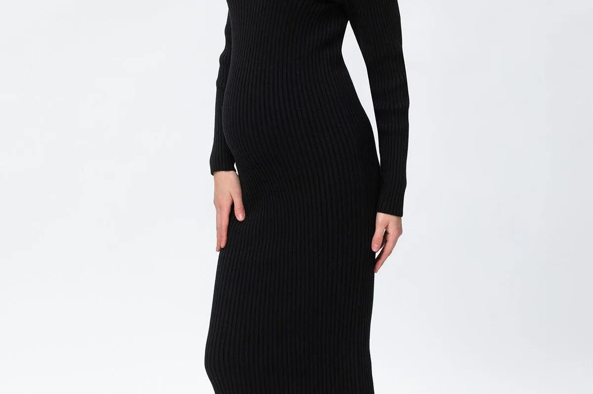 A woman modeling a black ribbed knit long-sleeve midi dress with a V-neckline, paired with taupe ankle boots, against a plain white studio background.
