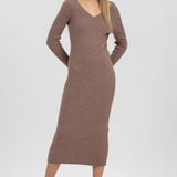 A woman modeling a ribbed knit long-sleeve midi dress in taupe brown, paired with dark brown patent leather ankle boots, against a light gray studio background.