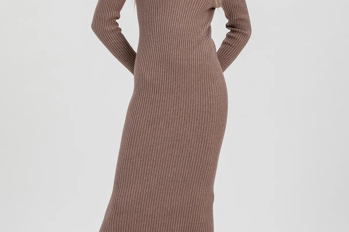 A woman modeling a ribbed knit long-sleeve midi dress in taupe brown, paired with dark brown patent leather ankle boots, against a light gray studio background.