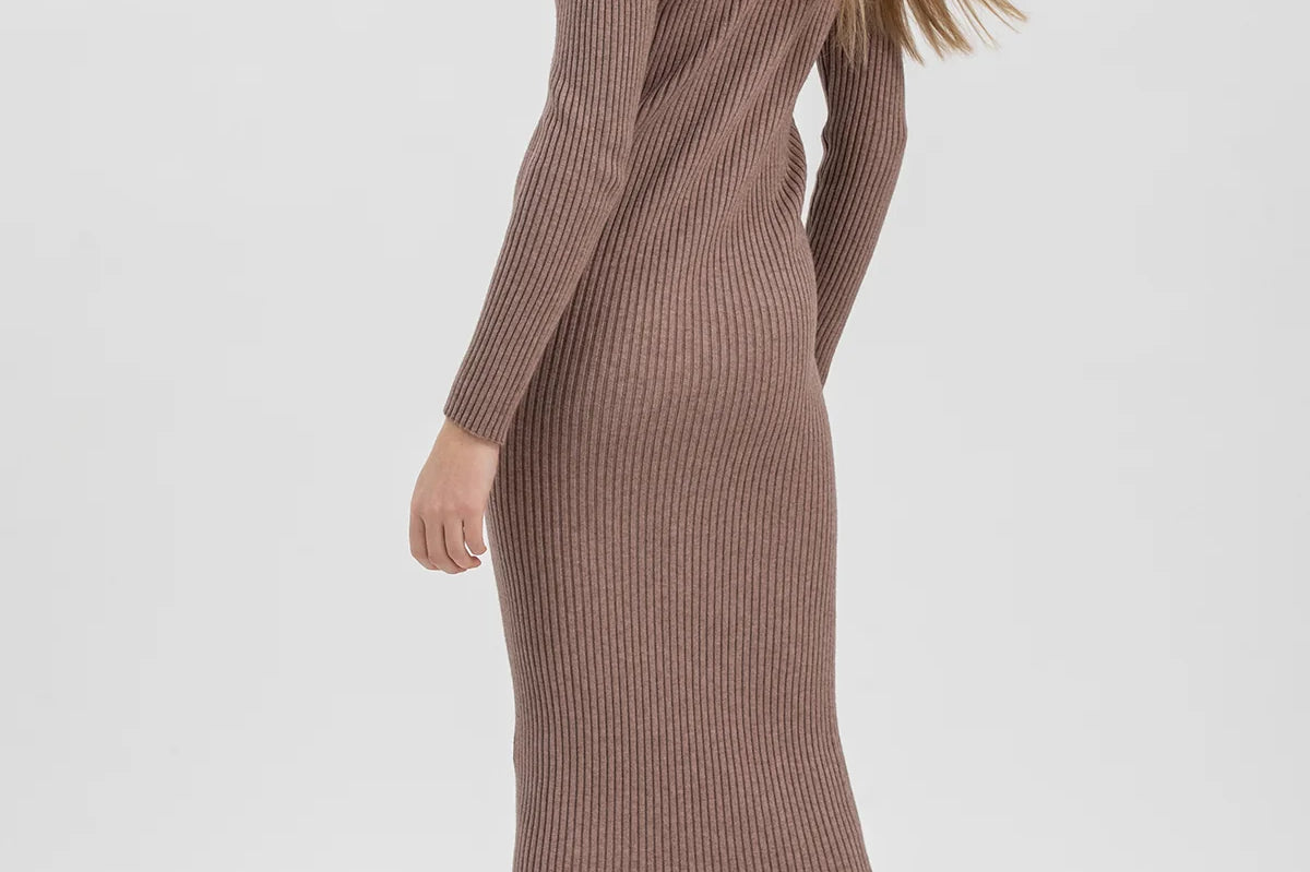 A woman modeling a ribbed knit long-sleeve midi dress in a muted taupe-brown color, paired with dark brown lace-up ankle boots, against a plain light gray studio background.