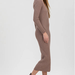 A woman modeling a ribbed knit long-sleeve midi dress in taupe brown, paired with dark brown patent leather ankle boots, against a light gray studio background.