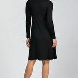A woman viewed from the back wearing a black long-sleeve ribbed knit dress and black heels against a light gray studio background.