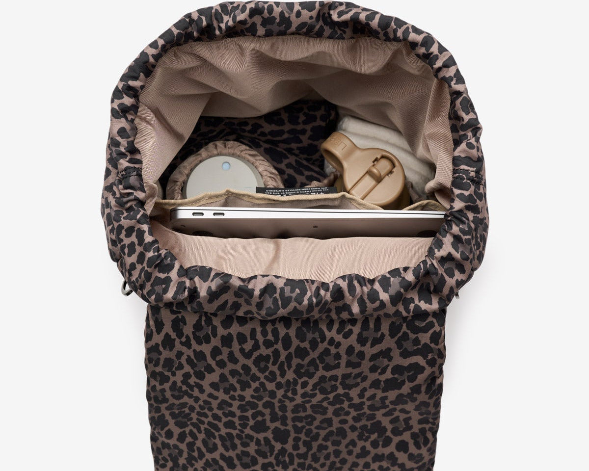 Leopard print baby bouncer with items inside on a white background