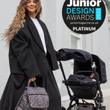 Woman in a black coat pushing a stroller with a leopard print bag, standing in front of a building. Junior Design Awards 2023 logo is visible.