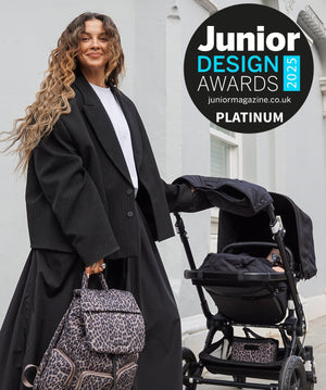 Woman in a black coat pushing a stroller with a leopard print bag, standing in front of a building. Junior Design Awards 2023 logo is visible.