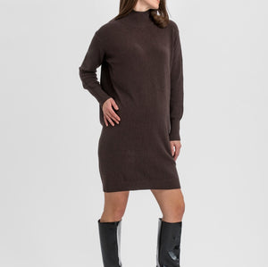 A woman modeling a dark brown ribbed knit mock-neck long-sleeve dress with black knee-high patent leather boots, standing against a light gray studio background.