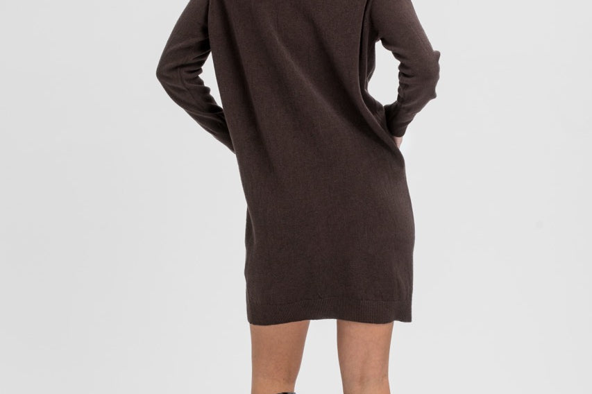 A woman shown from the back wearing a dark brown long-sleeve knit dress with a mock neck and black knee-high heeled boots, photographed against a light gray studio background.