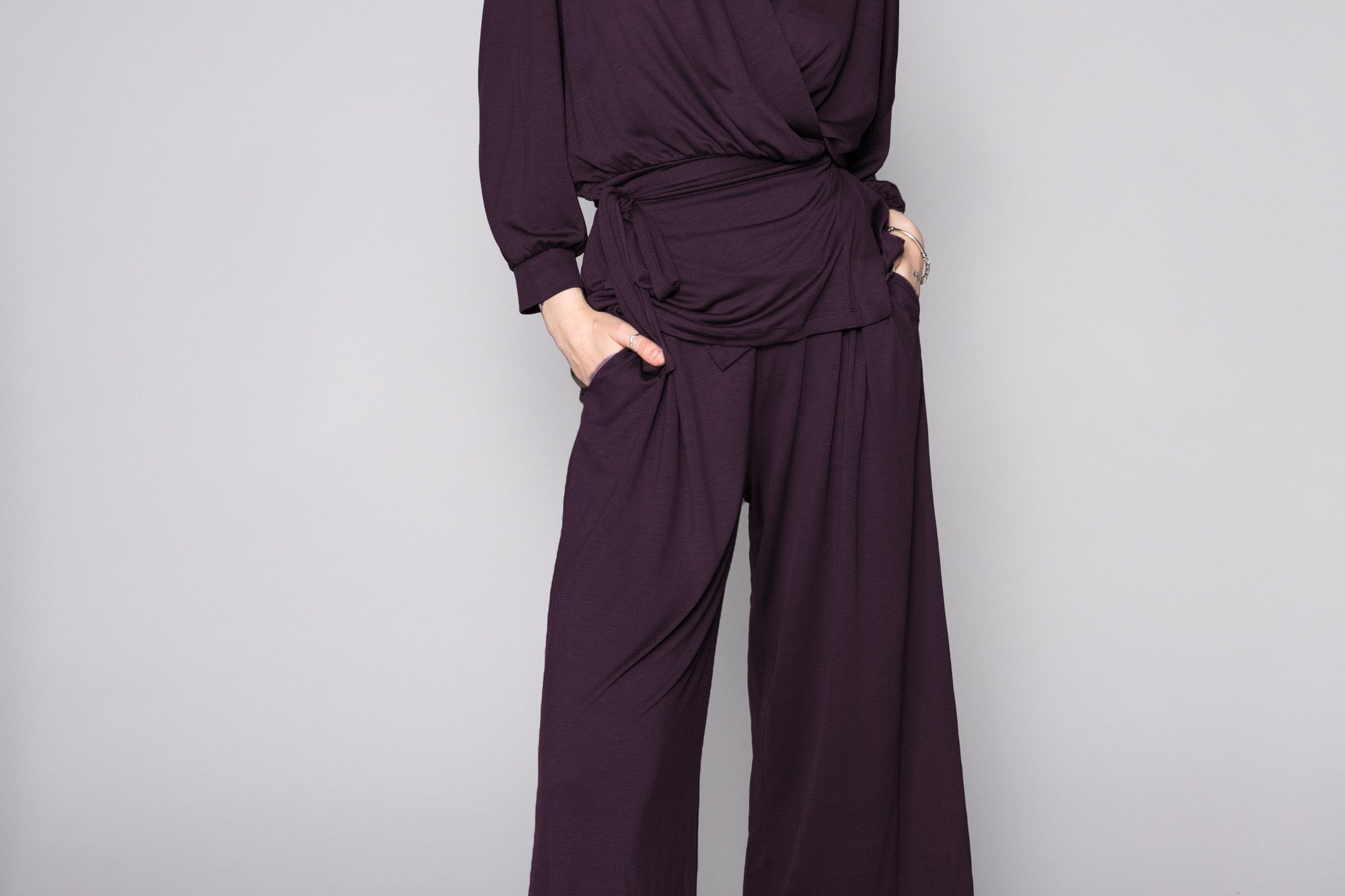 Person wearing a dark purple outfit with wide-leg pants on a gray background