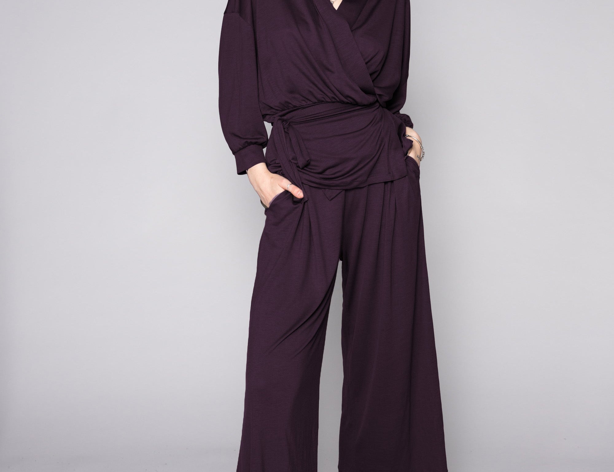 Person wearing a dark purple outfit with wide-leg pants on a gray background