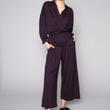 Person wearing a dark purple outfit with wide-leg pants on a gray background