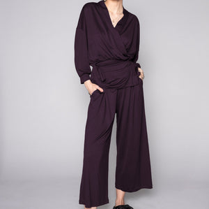 Person wearing a dark purple outfit with wide-leg pants on a gray background