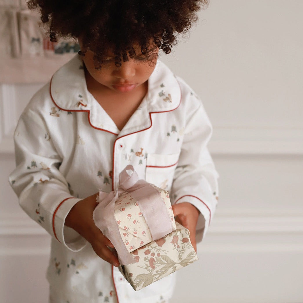 Child in pajamas holding a small gift box with a floral pattern.