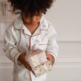 Child in pajamas holding a small gift box with a floral pattern.