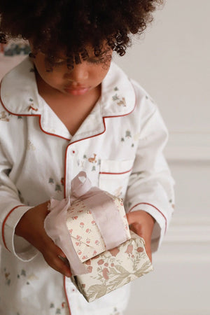Child in pajamas holding a small gift box with a floral pattern.