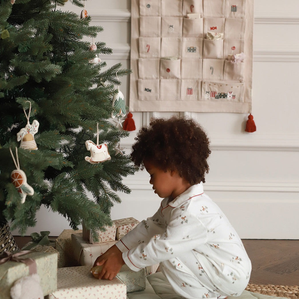 Child in pajamas opening a gift near a decorated Christmas tree with an advent calendar in the background.