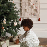 Child in pajamas opening a gift near a decorated Christmas tree with an advent calendar in the background.