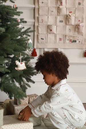 Child in pajamas opening a gift near a decorated Christmas tree with an advent calendar in the background.