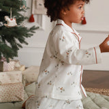 Child in pajamas standing in a room with a Christmas tree and presents.