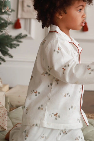 Child in pajamas standing in a room with a Christmas tree and presents.