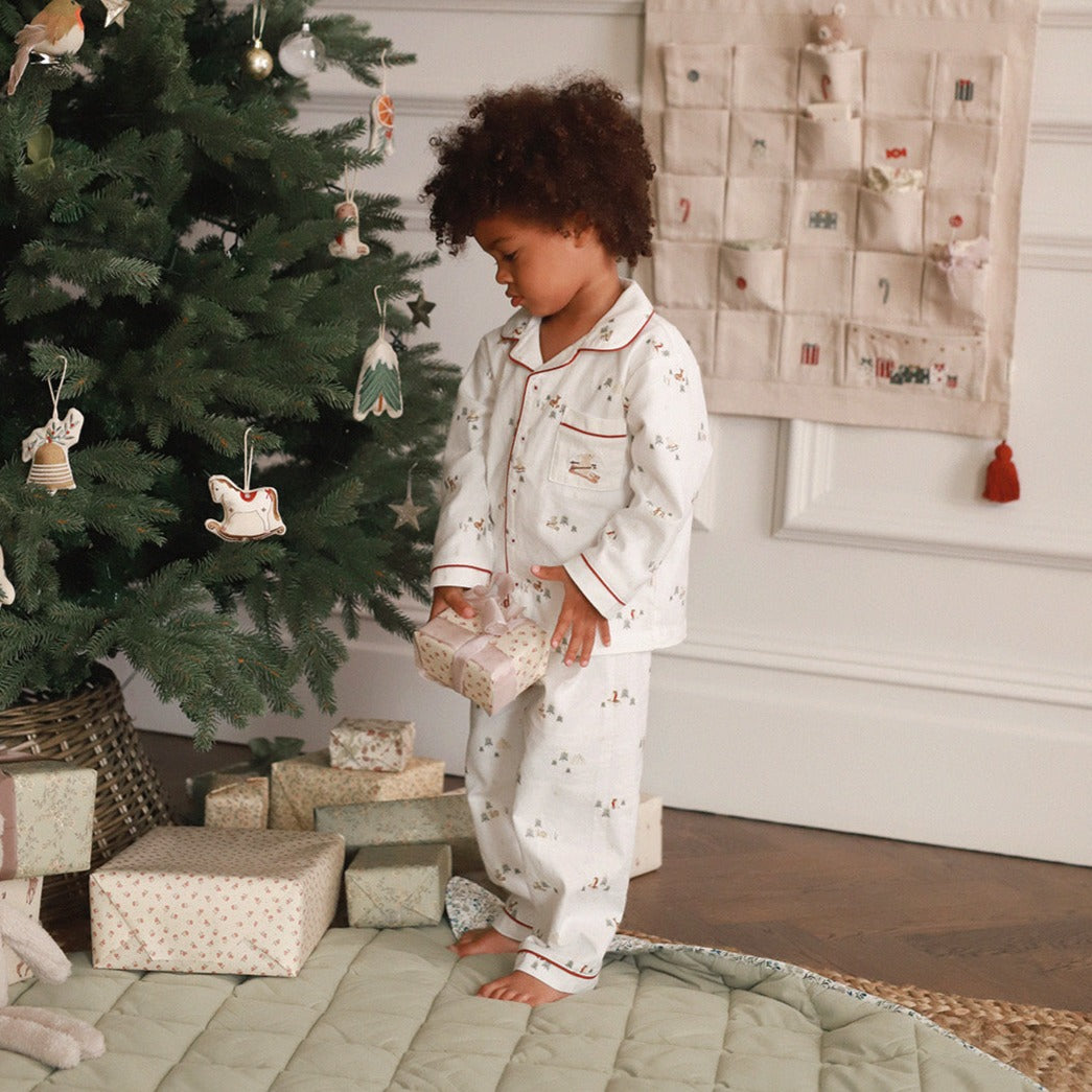 Child in pajamas standing next to a decorated Christmas tree with presents underneath.