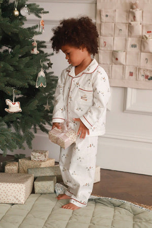 Child in pajamas standing next to a decorated Christmas tree with presents underneath.