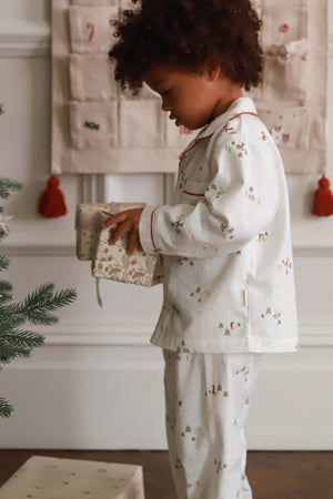 Child in pajamas holding a gift near a decorated Christmas tree.