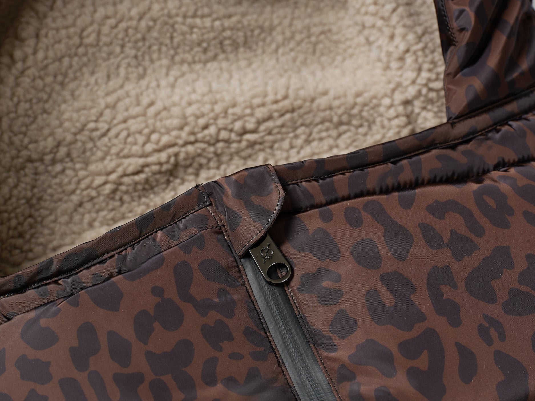 Close-up of a brown and black leopard-print puffer jacket with a beige sherpa fleece lining and a black zipper.