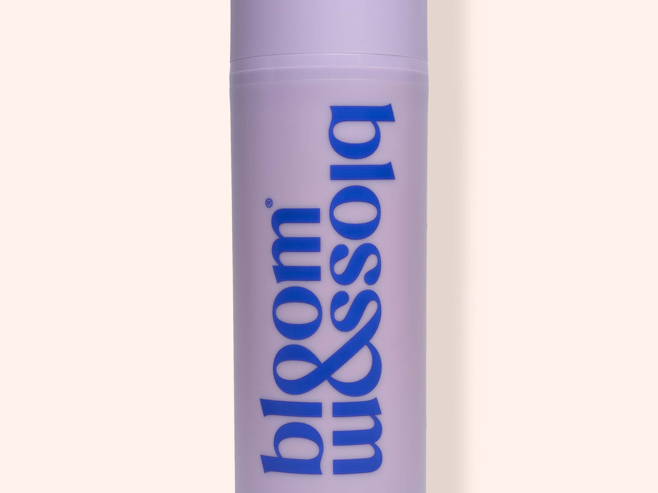 A lavender cylindrical bottle of bloom & soia Stretch Mark Cream with blue lettering, set against a solid pale peach background.