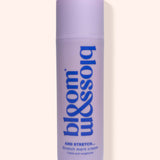A lavender cylindrical bottle of bloom & soia Stretch Mark Cream with blue lettering, set against a solid pale peach background.