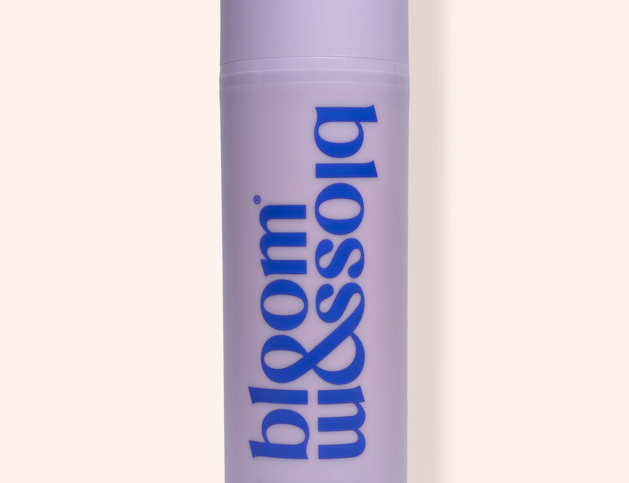 A lavender cylindrical bottle of bloom & soia Stretch Mark Cream with blue lettering, set against a solid pale peach background.