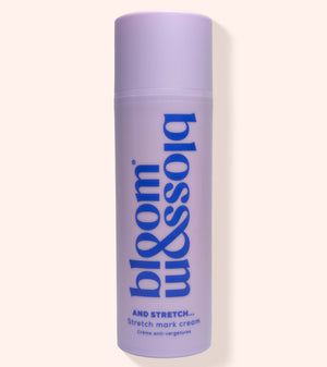 A lavender cylindrical bottle of bloom & soia Stretch Mark Cream with blue lettering, set against a solid pale peach background.