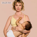 A woman wearing a pale yellow nursing bra holds a baby against her chest. The photo has a text label in the top-left corner that reads 'Chloe - 34D - Size M Breastfeeding - 12 months'.