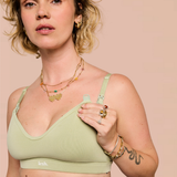 A woman wearing a sage green ribbed underwire bra with adjustable straps, shown in a close-up shot against a solid pale pink background. The brand name 'lesh.