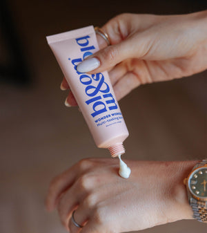 A close-up of a person squeezing a pink tube of lip & cheek tint onto the back of their hand. The tube has blue text that reads 'lip & cheek' and 'WONDER WORLD MULTI-REVIEW TINT'.