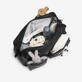 Open black backpack with baby items including a bottle, toys, and diapers on a white background
