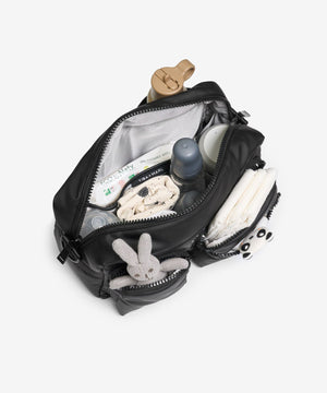 Open black backpack with baby items including a bottle, toys, and diapers on a white background